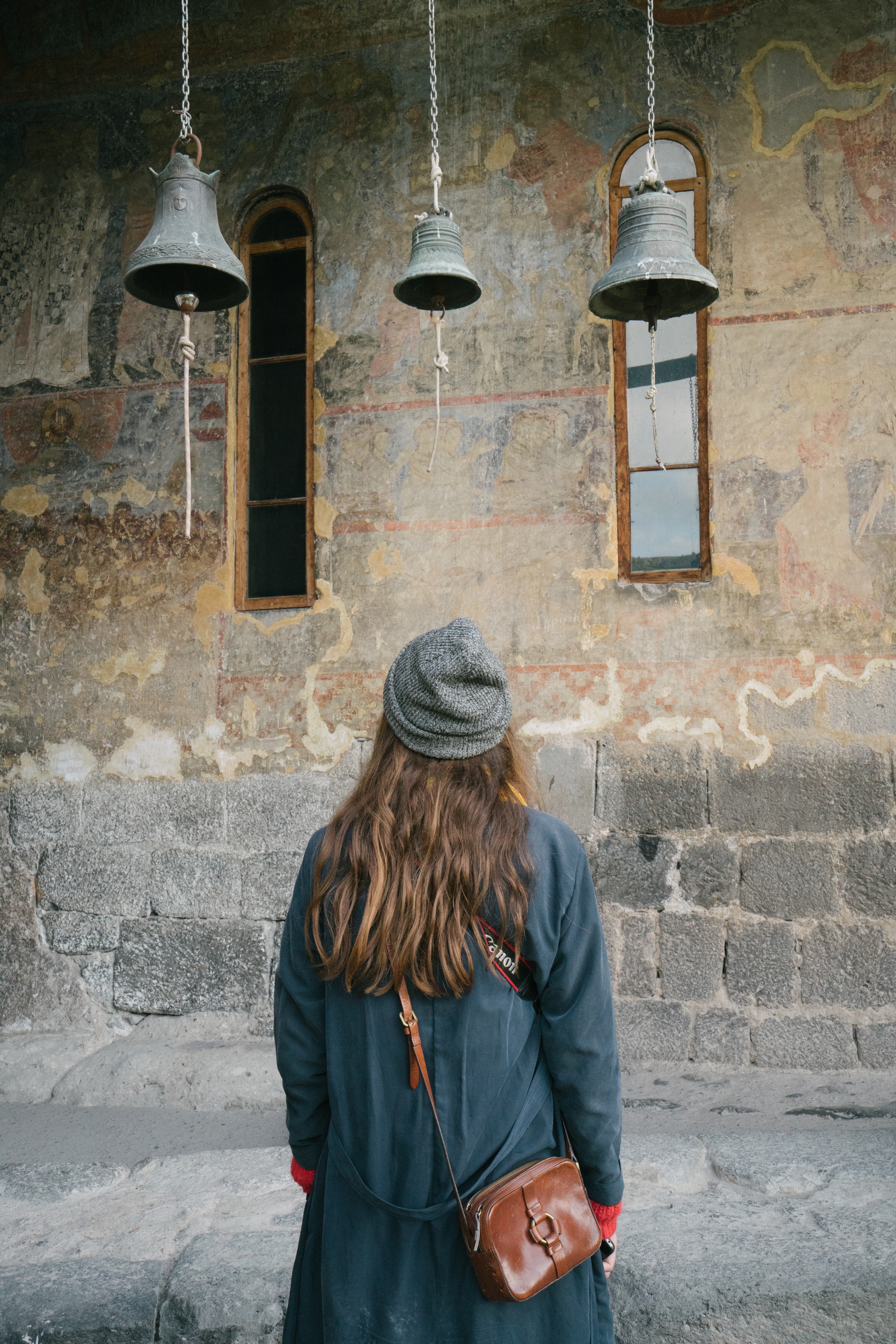 Une femme regardant avec émerveillement trois cloches suspendues dans une église ancienne.