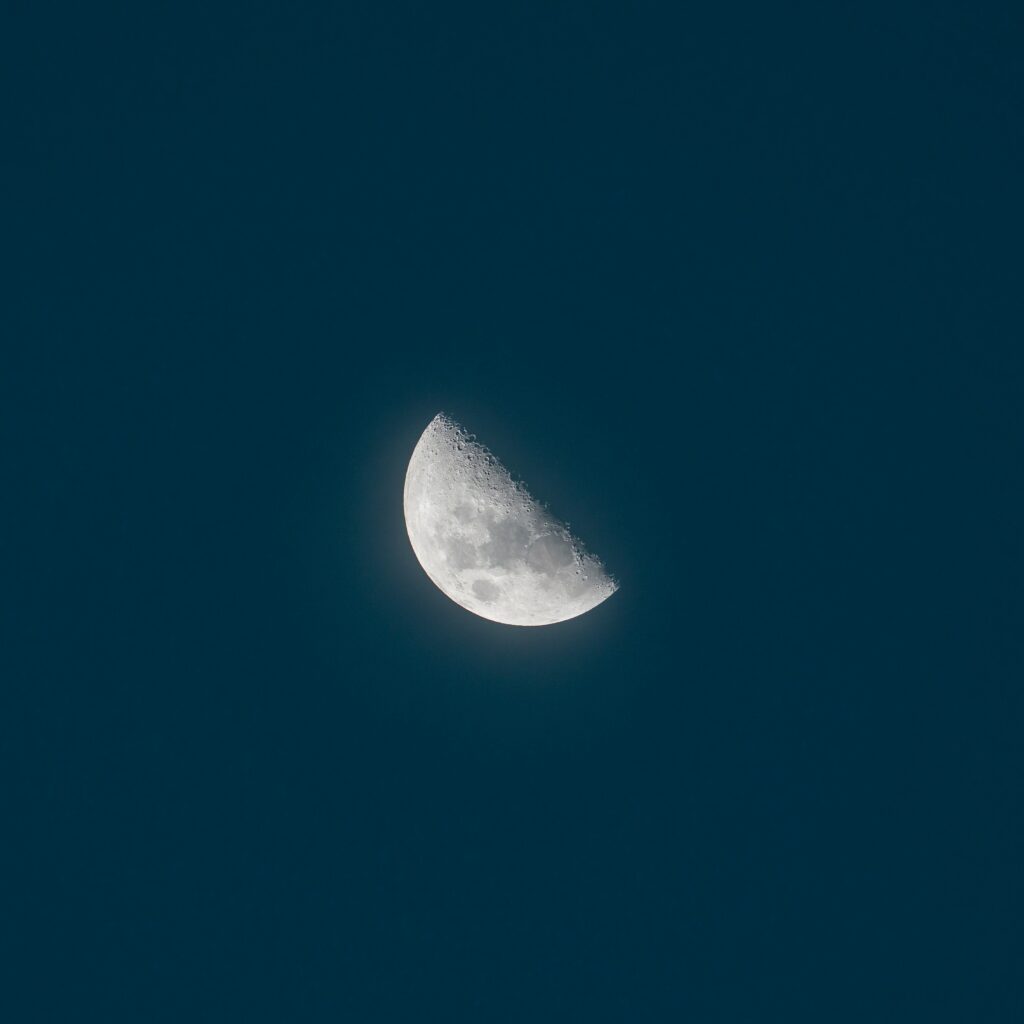 Photo d'une demi-lune magnifiquement zoomée, flottant dans le ciel nocturne étoilé. La lumière argentée de la lune coupe le ciel en deux, évoquant une mystérieuse présence dans l'obscurité. L'image souligne la beauté de la demi-lune et son importance en tant que symbole de féminité, d'intuition et de mystère. Elle nous invite à réfléchir à la signification spirituelle de la demi-lune et à sa place dans nos vies