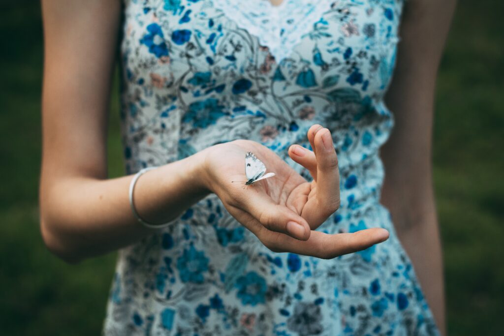 Une femme portant une robe fleurie tient délicatement un papillon blanc dans sa main, symbolisant la signification spirituelle d'un papillon blanc apparaissant dans la maison