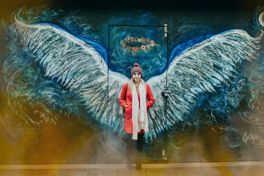 Une femme se tient devant un mur avec deux ailes dessinées qui semblent être les siennes, symbolisant l'éveil spirituel.