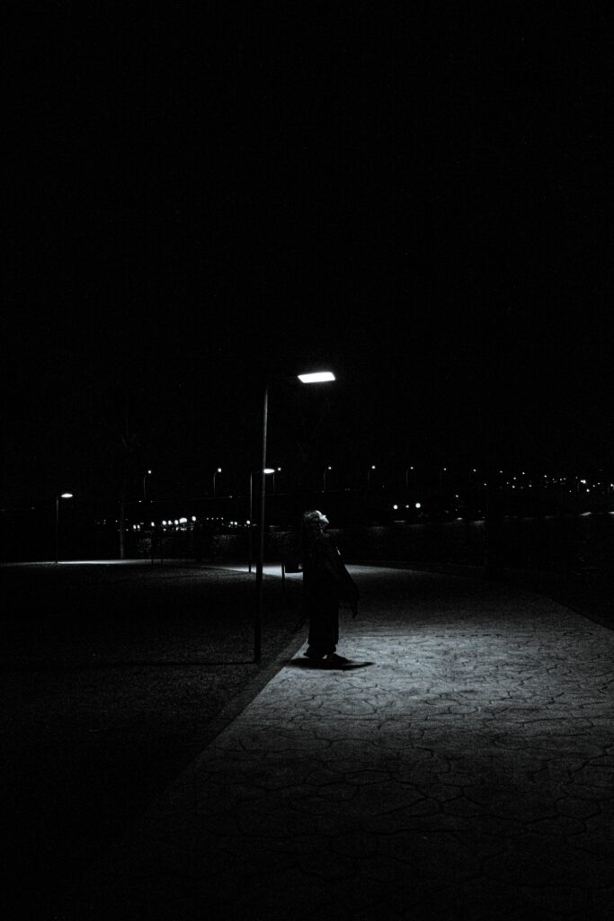 Femme mystérieuse sous une lampe de rue illuminée la nuit, illustrant la signification spirituelle d'une lampe de rue qui s'allume