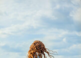 Une femme blonde récoltant de la lavande dans un panier en paille dans un champ de lavande sous un ciel bleu clair