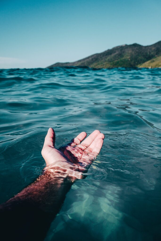 Une main touchant délicatement la mer depuis la plage, symbolisant les défis de la vie illustrés par les tempêtes en mer