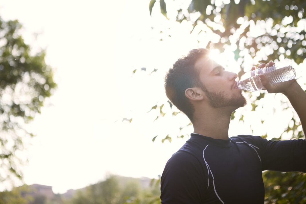 Un homme sous un soleil éclatant boit de l'eau, le visage marqué par la chaleur d'une journée particulièrement chaude